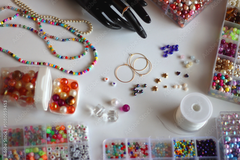 Fototapeta premium Hand figurine, colorful friendship bracelets, necklaces, various beads and DIY supplies on the table. Making jewelry at home. Selective focus.