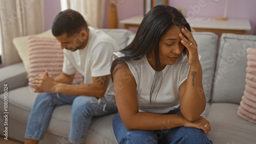 Hispanic couple sitting on a couch in a living room looking sad and distressed indoors