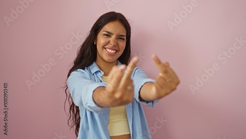 Fotografie Beautiful young hispanic woman making an offensive gesture with both middle fingers while smiling, standing against an isolated pink background wall