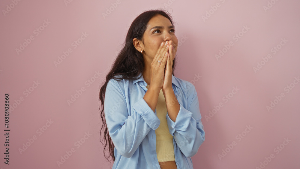 Young, attractive, hispanic woman with long brunette hair covers her mouth with her hands, standing over an isolated pink background wall, wearing a light blue shirt. Young, attractive, hispanic woman with long brunette hair covers her mouth with her hands, standing over an isolated pink background wall, wearing a light blue shirt.