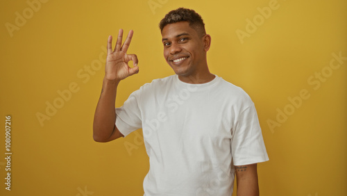 Handsome young hispanic man smiling and making an okay gesture isolated over a vibrant yellow background