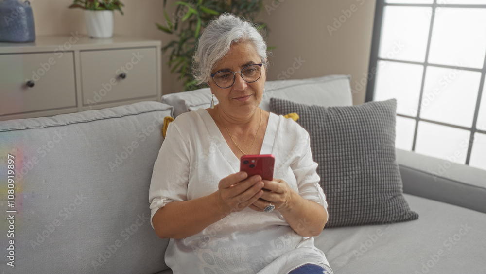 Elderly woman with grey hair using smartphone at home sitting on a sofa in a living room looking content and relaxed Elderly woman with grey hair using smartphone at home sitting on a sofa in a living room looking content and relaxed