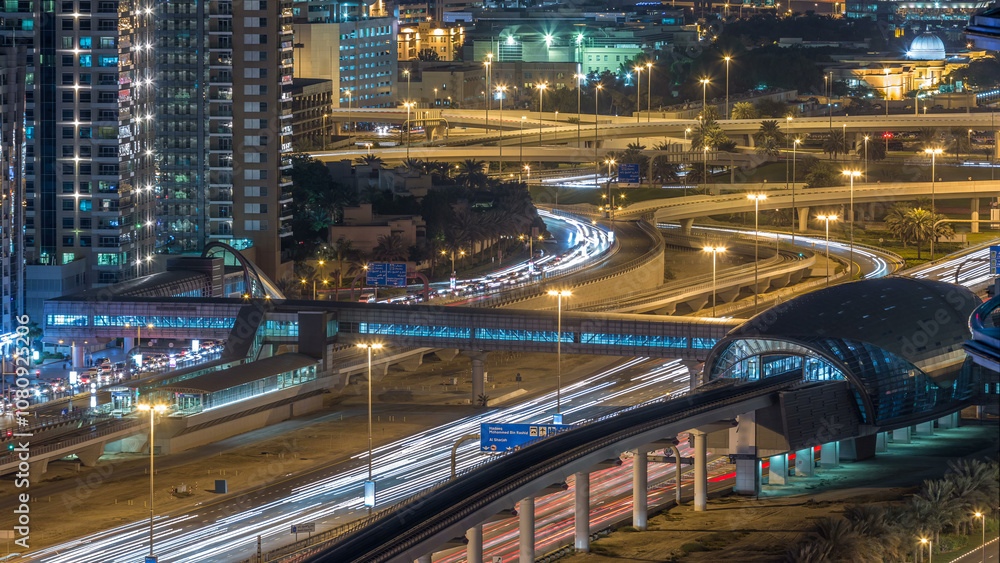 Fototapeta premium Futuristic building of Dubai metro and tram station and luxury skyscrapers behind night timelapse