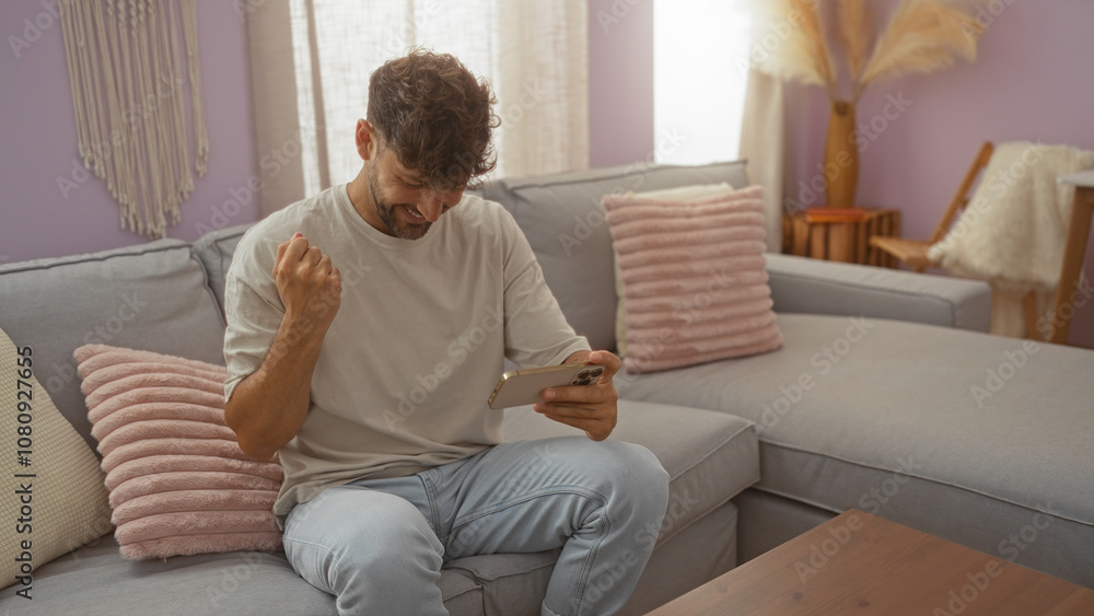 Young man sitting in a living room holding a phone and looking excited, surrounded by pillows and modern decor Young man sitting in a living room holding a phone and looking excited, surrounded by pillows and modern decor