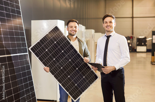 Portrait of a happy male consultant and customer holding a solar panel in a hardware shop. Promoting renewable energy solutions, showcasing solar power as a sustainable electricity source. photo