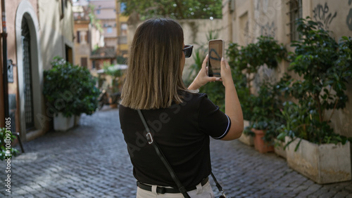 Photography Woman taking photo on smartphone in picturesque rome street with vibrant greenery, showcasing italian architecture and lively urban vibes in historic old town