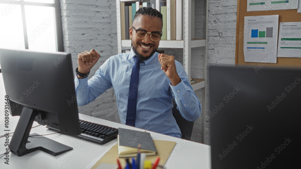 Young man with braids and glasses in office celebrates success at computer desk indoors looking happy and professional Young man with braids and glasses in office celebrates success at computer desk indoors looking happy and professional