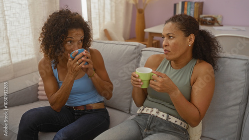 Latina women enjoying coffee and conversation in a cozy living room setting, emphasizing friendship, relaxation, and home comfort. photo