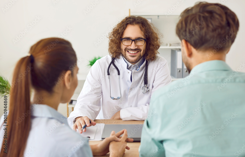 Friendly male doctor advises married couple on pregnancy management and gives them prenatal advice. Portrait of smiling male obstetrician gynecologist consulting couple sitting with backs to camera. Friendly male doctor advises married couple on pregnancy management and gives them prenatal advice. Portrait of smiling male obstetrician gynecologist consulting couple sitting with backs to camera.