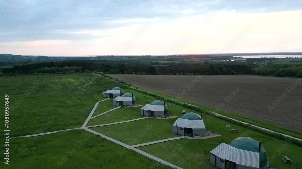 Morning sunrise view from a dens forest and some tent house on a grass field Morning sunrise view from a dens forest and some tent house on a grass field