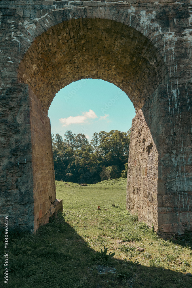 View through ancient stone archway to green meadow and trees View through ancient stone archway to green meadow and trees