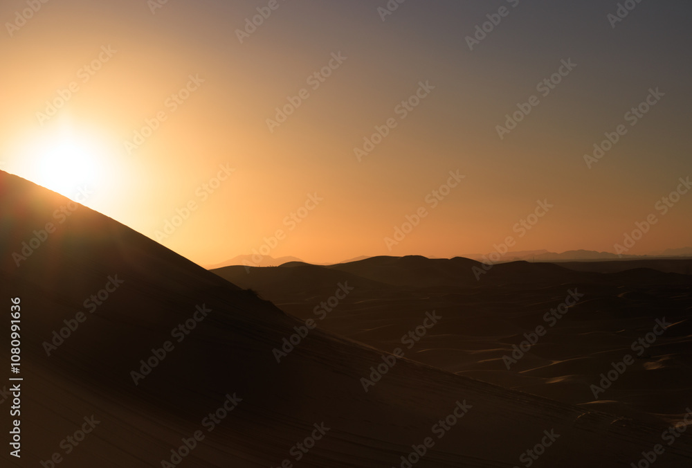 Backlit sand dunes desert landscape at sunset, with tourists on the horizon.  Erg Chebbi. Merzouga. Sahara. Morocco. Africa.