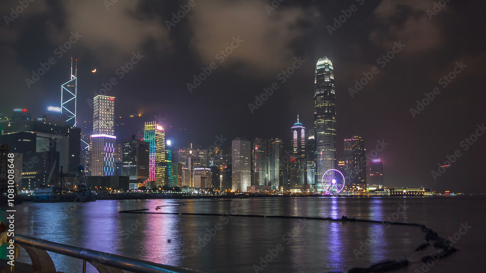 Obraz premium Hong Kong city skyline at night over Victoria Harbor with cloudy sky and urban skyscrapers timelapse hyperlapse.