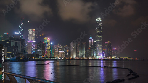 Hong Kong city skyline at night over Victoria Harbor with cloudy sky and urban skyscrapers timelapse hyperlapse.