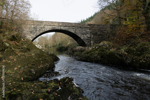 Pont yr Afanc bridge arching over the river Conwy in a forest against a misty sky