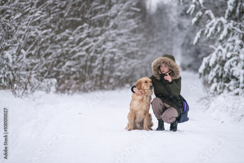 Beautiful young girl walking with a purebred retriever near a snowy forest in winter.