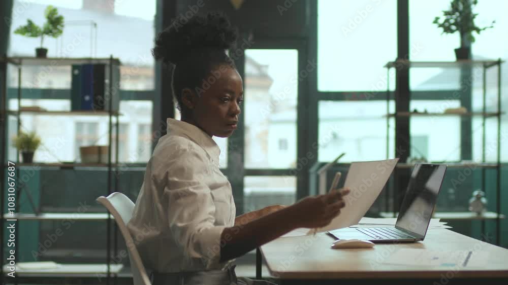 Attractive African American woman sitting on chair use laptop work with paper in office. Serious. Camera moving around. 360 degrees