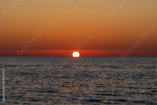 Marina di Pisa, Province of Pisa, Italy - November 4, 2024:  The sun sets against the sea. Reflection of the sun in the sea water. photo