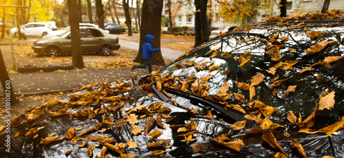 Close-up of dry brown leaves covering a car windshield in an urban setting during autumn. Reflecting the calm and nostalgic vibe of fall in the city, ideal for seasonal or nature concepts.