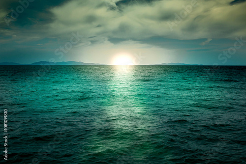 Emerald green sea with sun and cloudy sky background, calm ocean water surface, relaxing sunset or sunrise morning atmosphere, dark natural texture reflection.