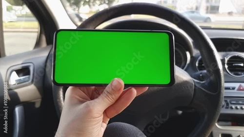 Female hand holding horizontal green screen smartphone in car with busy road background. Mockup for advertising the novigator, carsharing and other applications. photo