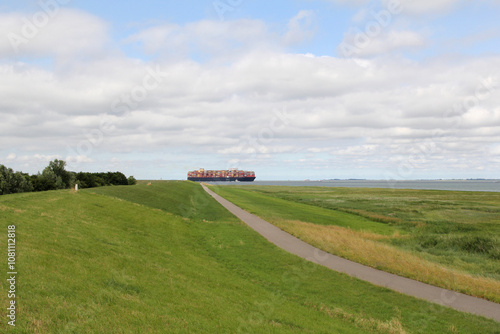 a coast landscape with a big container ship in the westerschelde sea and a green seawall and salt marsh in front photo