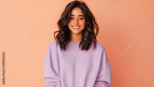 A smiling young woman in a pastel sweater against a peach background.