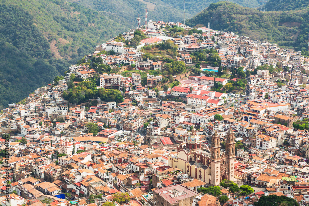 Fototapeta premium Aerial panoramic view over Pueblo Magico of Taxco, one of Mexico's most scenic towns with Santa Prisca church and a scenic mountainous landscape. Taxco, Guerrero, Mexico