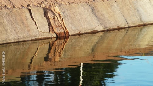 The crumbling concrete bank of a water-filled canal in the morning, part of the Central Arizona Project in Phoenix, Arizona