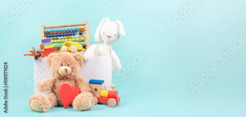 Toy box full of baby kid toys. Container with teddy bear, fluffy and educational wooden toys on light blue background. Cute toys collection for small children. Donation, toys store, giving tuesday