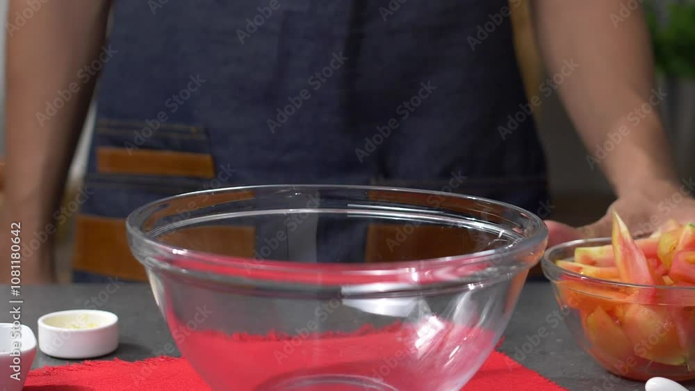 Chef in Slow Motion Serving Large Slices of Red Tomatoes, Transferring Them from a Small Transparent Bowl to a Larger One Placed on a Red Placemat. Healthy Food Concept. FullHD footage Chef in Slow Motion Serving Large Slices of Red Tomatoes, Transferring Them from a Small Transparent Bowl to a Larger One Placed on a Red Placemat. Healthy Food Concept. FullHD footage