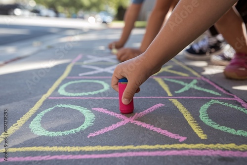 A child’s hands draw a colorful tic-tac-toe game on a concrete sidewalk using pastel chalks on a sunny day. A fun outdoor activity promoting creativity and play.