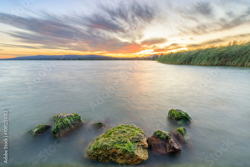 Sunset on Lake Balaton with green mossy stone with moss on it with reflection