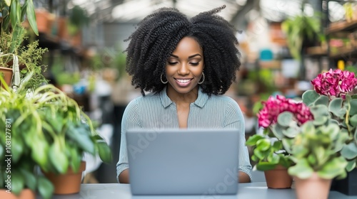 A cheerful woman works on her laptop in a lush greenhouse, surrounded by vibrant plants.