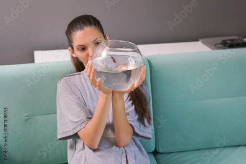 A woman gently cares for her vibrant fish in a glass bowl while focusing on the aquatic life around her in a cozy home photo