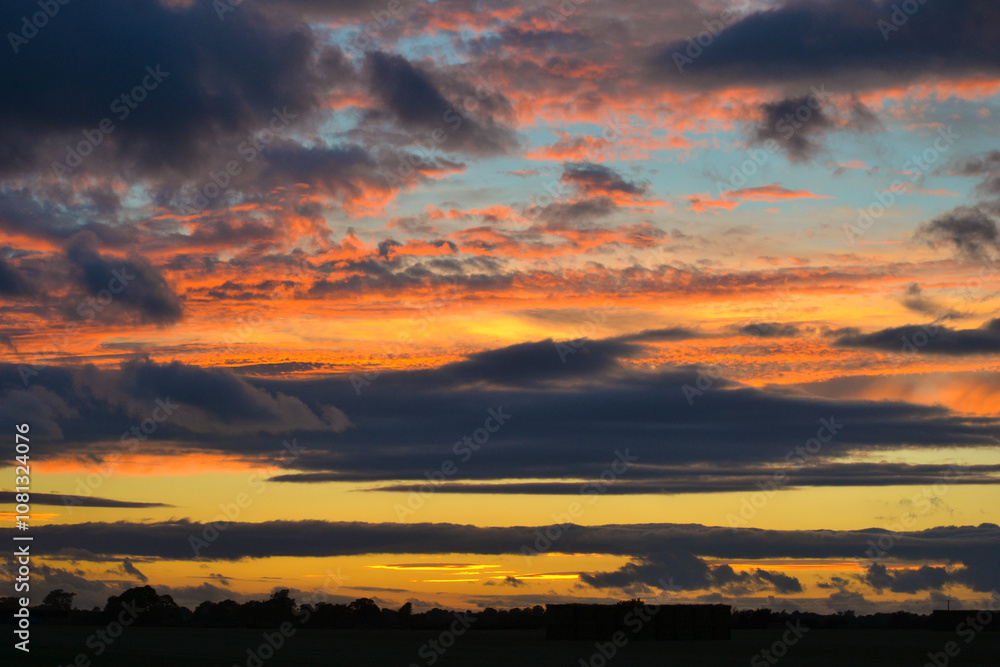 Vibrant Sunset Sky with Yellow and Blue Clouds Over a Tranquil Field Vibrant Sunset Sky with Yellow and Blue Clouds Over a Tranquil Field
