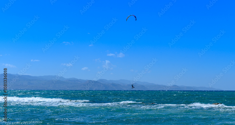 Kite surfer glides through vibrant blue waters under a clear sky at the coast during a sunny afternoon adventure Kite surfer glides through vibrant blue waters under a clear sky at the coast during a sunny afternoon adventure
