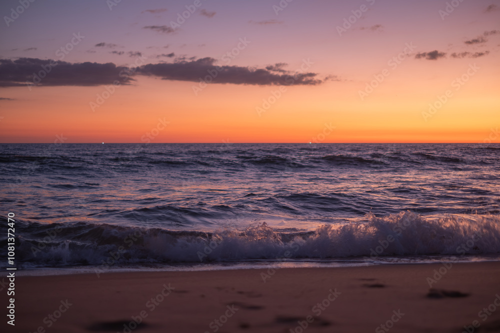 Fototapeta premium A serene sunset over the calm ocean waves at a peaceful beach, capturing the vibrant colors of dusk