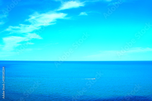 Peaceful scenery from Numana Alta with a vision of the vast Adriatic Sea and its slightly rippling waters crossed by a motorboat leaving a foamy white trail on their blue waves and a cyan horizon