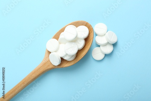 Antibiotic pills and spoon on light blue background, flat lay