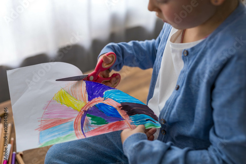 A young girl carefully cuts out her drawing with scissors, showcasing her creativity and focus.