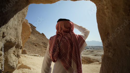 Saudi Arabian man coming out of cave and seeing desert landscape - medium shot