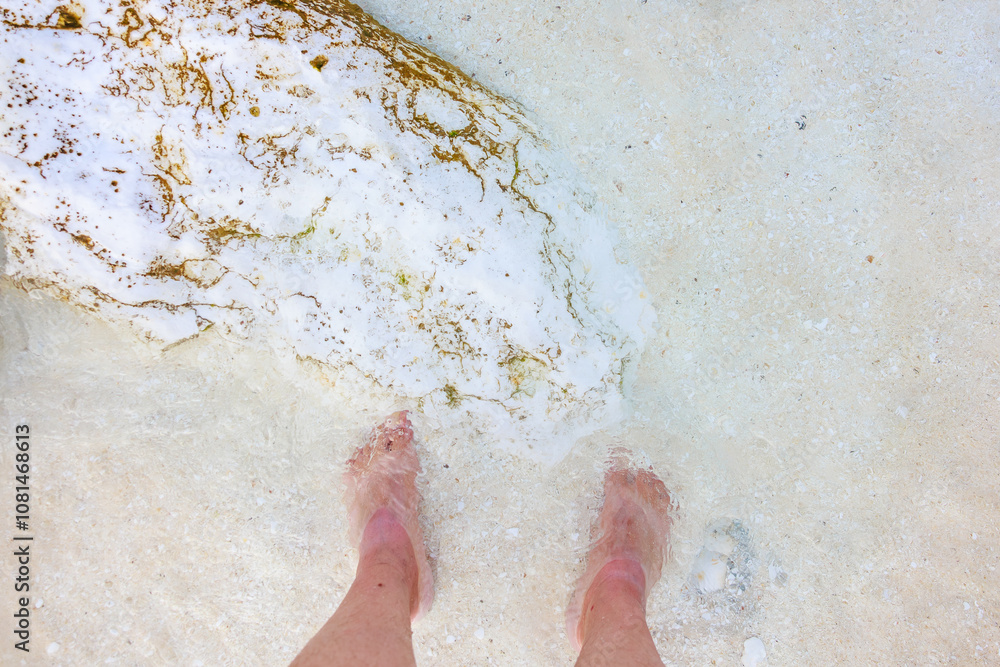 A person's feet are in the water, and the sand is white A person's feet are in the water, and the sand is white