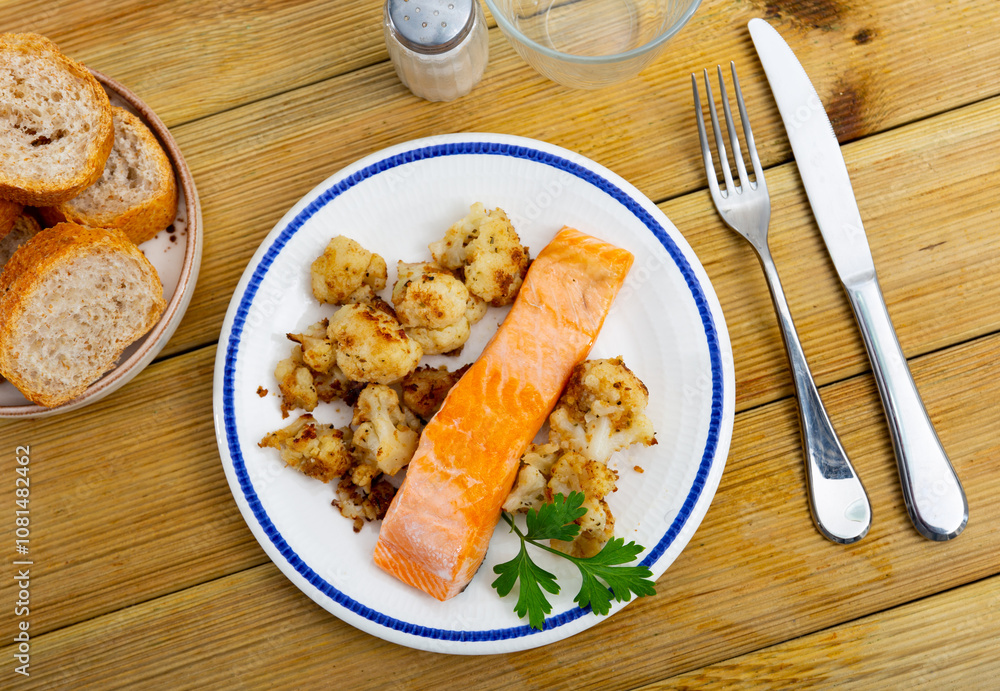 Cooked salmon fillet with cauliflower and parsley on a plate on a wooden table. Nutritious diet lunch with fish and vegetables Cooked salmon fillet with cauliflower and parsley on a plate on a wooden table. Nutritious diet lunch with fish and vegetables