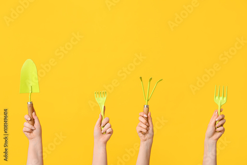 Female hands with gardening shovel and rakes on yellow background