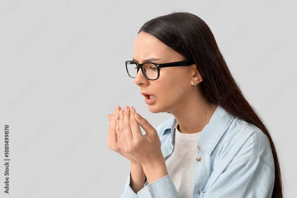 Beautiful young woman suffering from sore throat on grey background