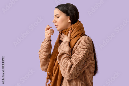 Beautiful young woman in scarf suffering from sore throat on lilac background photo