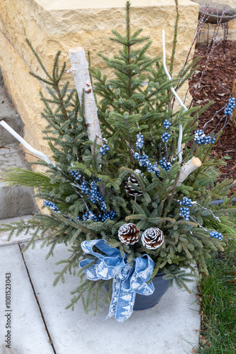 Festive outdoor Christmas holiday potted planter with decorations and a blue ribbon bow
