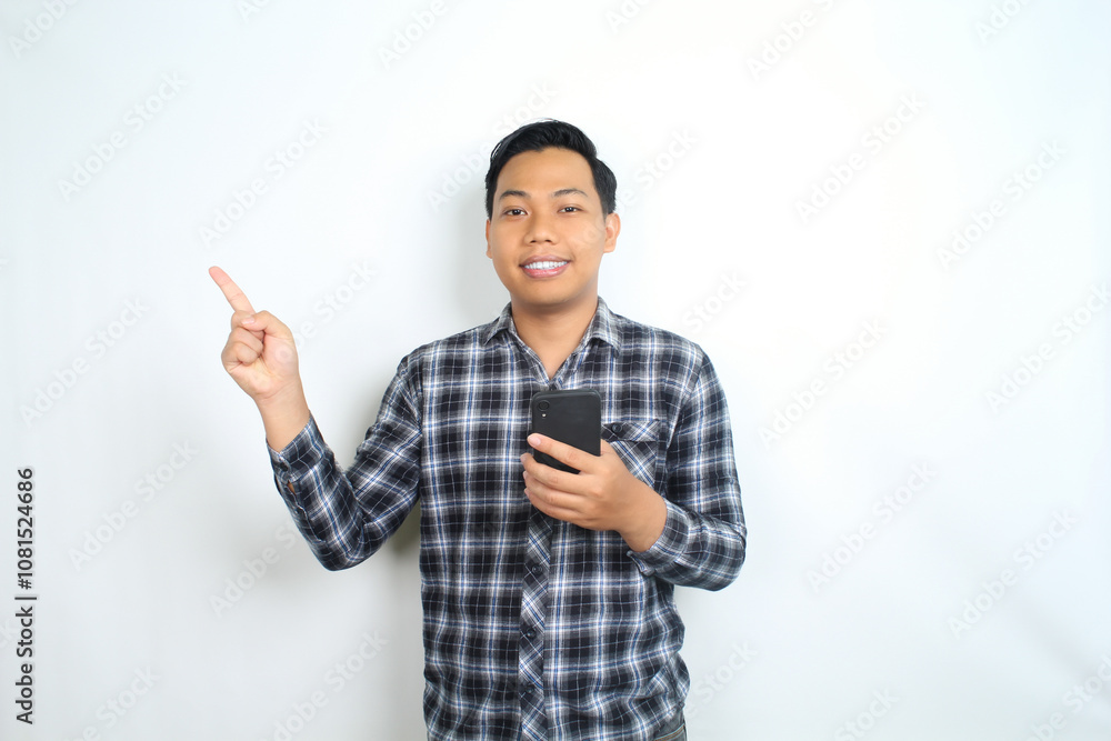 smiling asian man pointing to copy space with holding mobile phone isolated on white background smiling asian man pointing to copy space with holding mobile phone isolated on white background