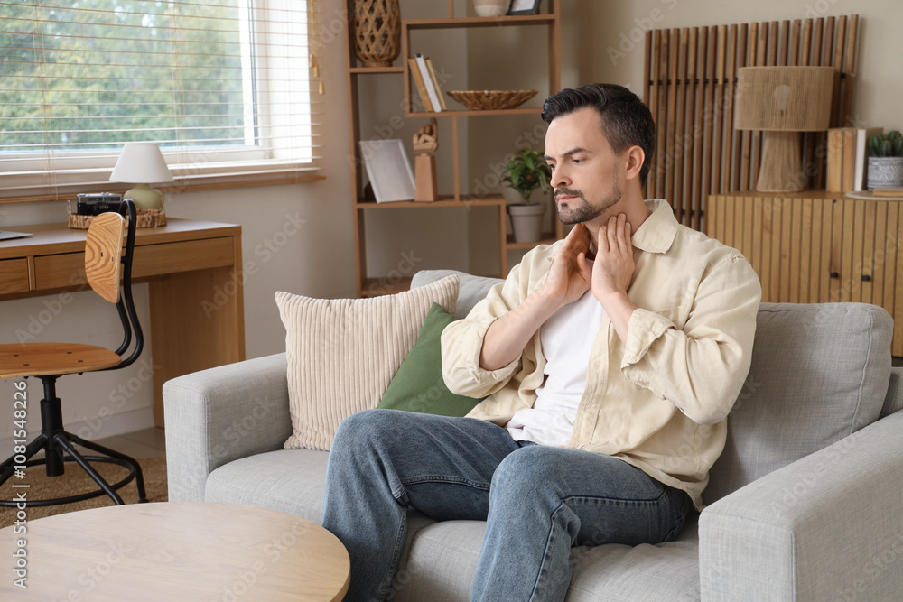 Handsome man self-examining thyroid gland on sofa at home Handsome man self-examining thyroid gland on sofa at home